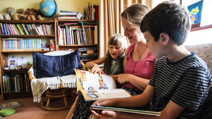 Sarah Nicholson  at home in Myrniong sitting on the couch reading to her two children.