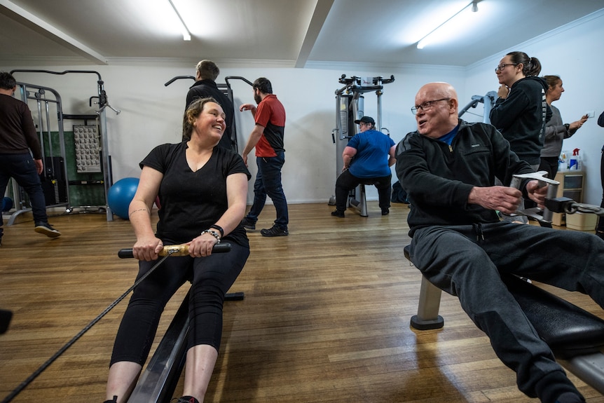 A man and a woman on a rowing machine next to each other.