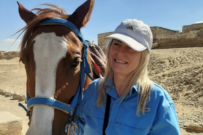 Jill Barton smiling next to a horse with the sandy Egyptian landscape behind her.