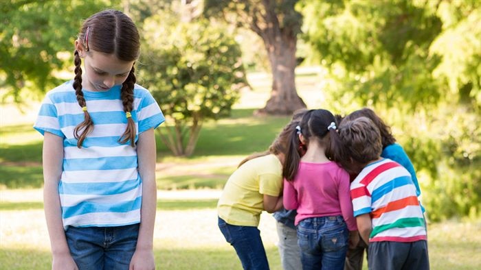A child is seen excluded from a group of her peers.