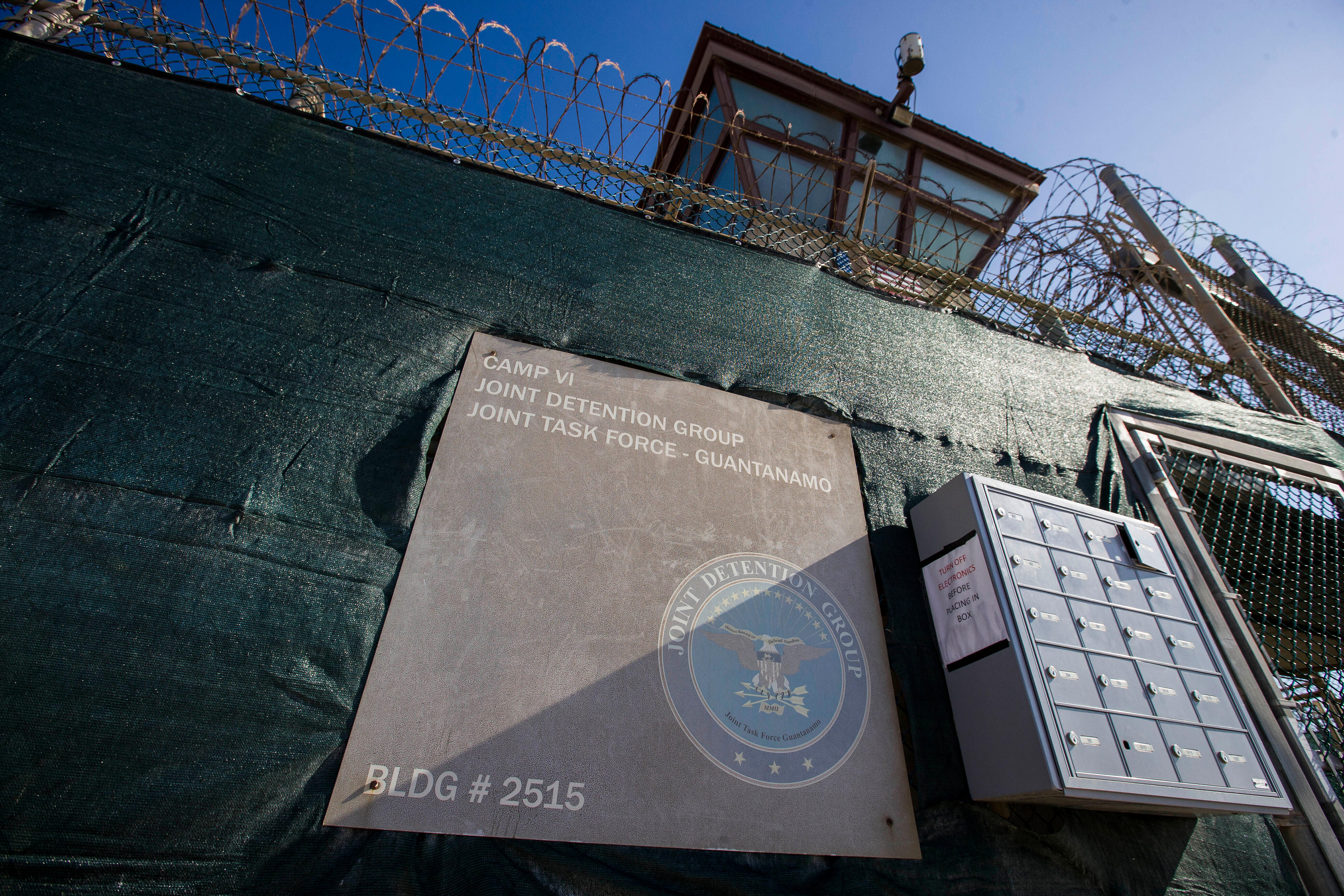 The side of a prison building with barbed wire at the top and a sign in front