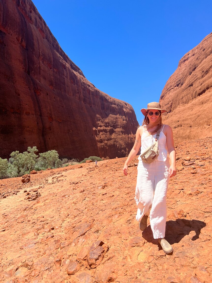 Bright red rock formations with a young woman with long hair wearing white in the centre of the image.