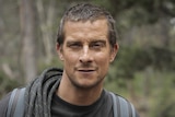 Survivalist Bear Grylls in the wilderness with a coil of rope over his shoulder and a hawk-like expression on his face.