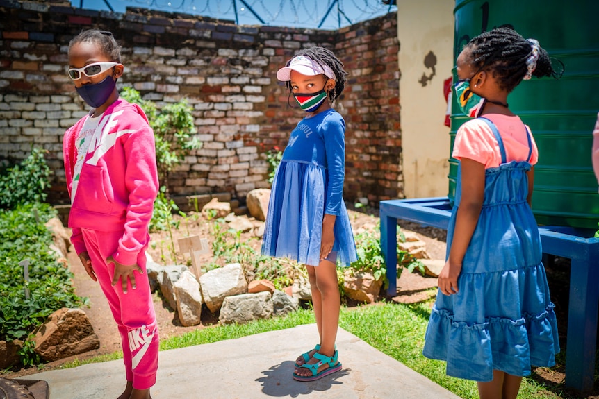 Three little girls in South Africa in a socially distanced line outside a school 