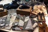 A group of items on a table including t-shirts in plastic bags, shoes, bags and a watch.