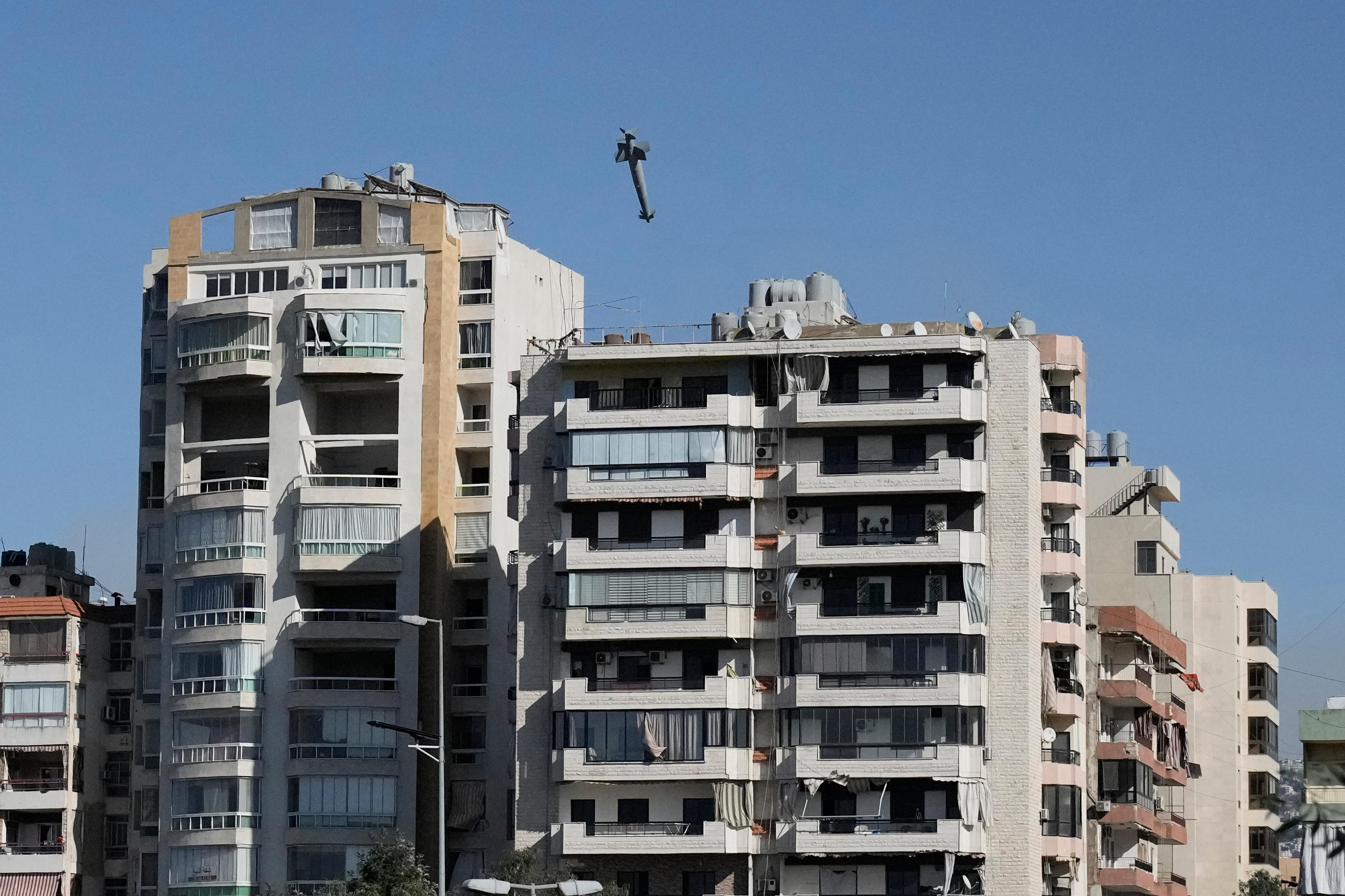 A large grey missile flies over two multi-storey residential buildings. 