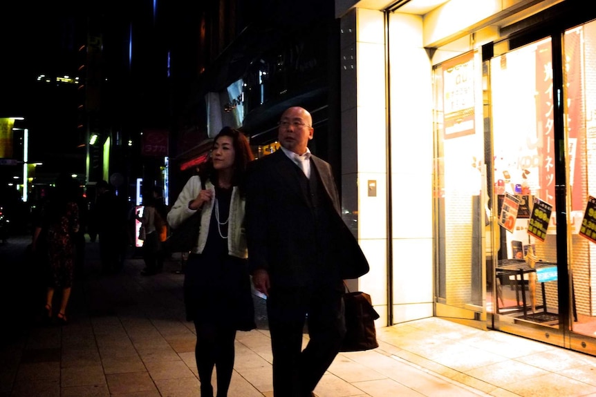 Couple walk arm in arm in front of a closed shop.