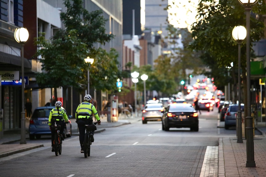 Two fluorescent yellow clad police officers on bicycles patrol Hay Street in Perth' CBD at dusk