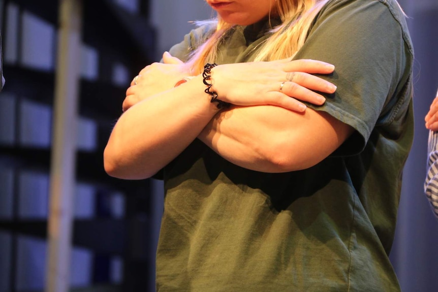 A woman stands on a makeshift stage at Dame Phyllis Frost, arms folded.