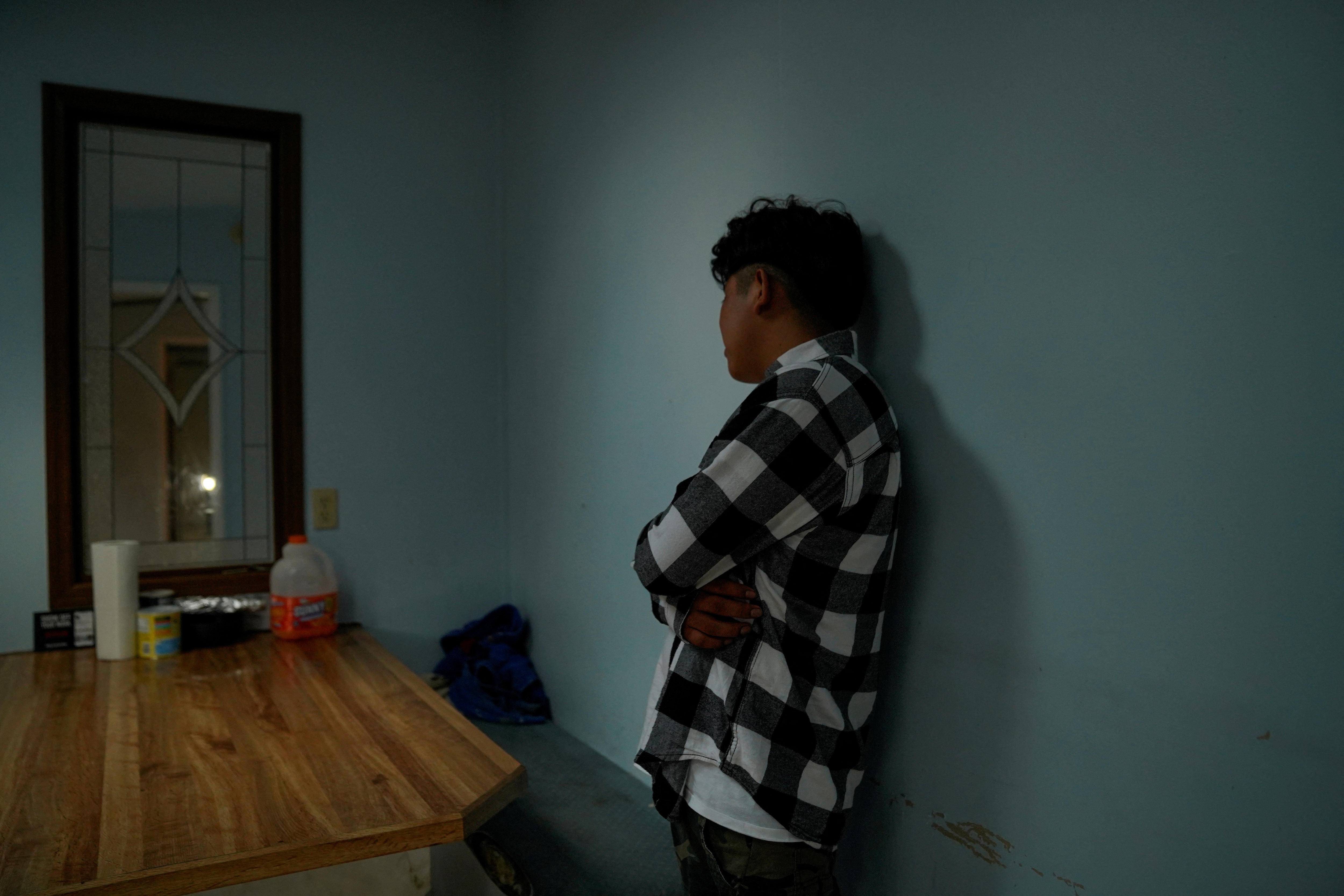 una persona con una camisa a cuadros se para contra una pared de una casa con la espalda girada hacia la cámara oscureciendo su cara