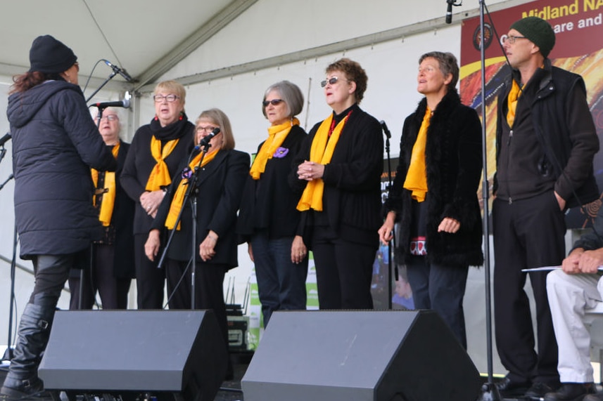 About eight members of the Madjitil Moorna Choir stand on stage singing in front of co-founder Della Rae Morrison.