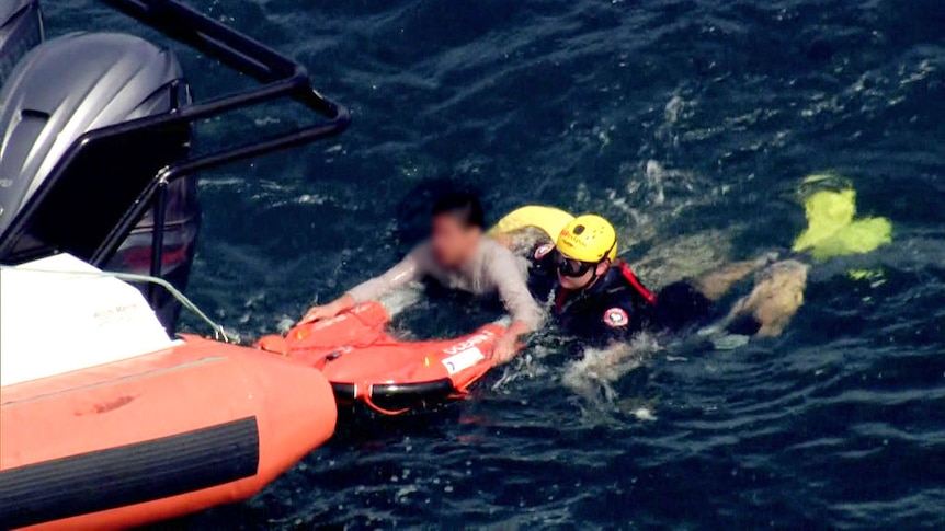 Man holds on to floatation device attached to rubber rescue boat. He is accompanies by a rescue worker.