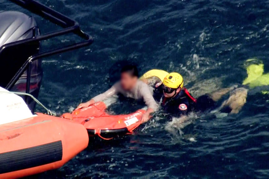 Man holds on to floatation device attached to rubber rescue boat. He is accompanies by a rescue worker.