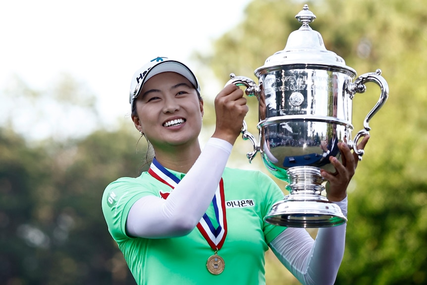 Una sonriente Minjee Lee lleva una medalla alrededor del cuello mientras levanta una copa de plata después de ganar el US Women's Open.  