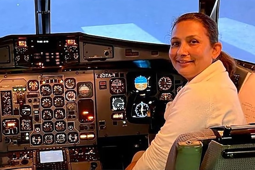A Nepalese woman in a white uniform sits at the controls of an airplane.