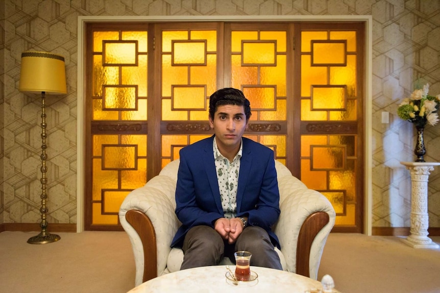 Still image from 2017 film Ali's Wedding of lead actor Osamah Sami seated with tea and looking towards the camera.