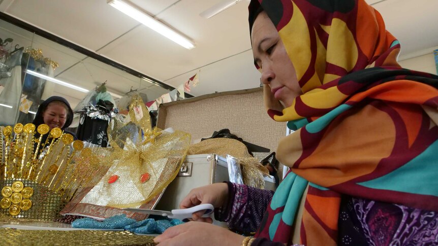 Woman wearing headscarf and dressed very colourfully about to cut some fabric