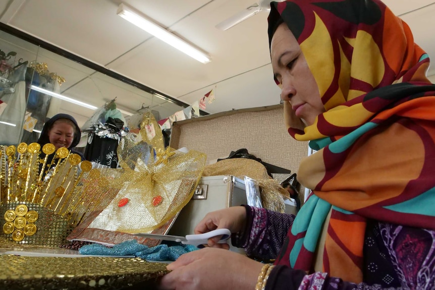 Woman wearing headscarf and dressed very colourfully about to cut some fabric