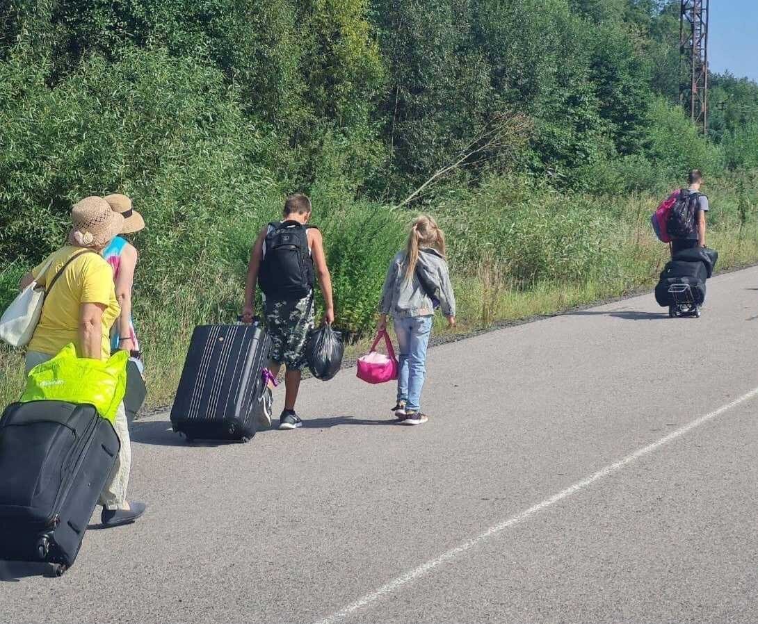 People walk down the street carrying luggage as they leave occupied territories. 