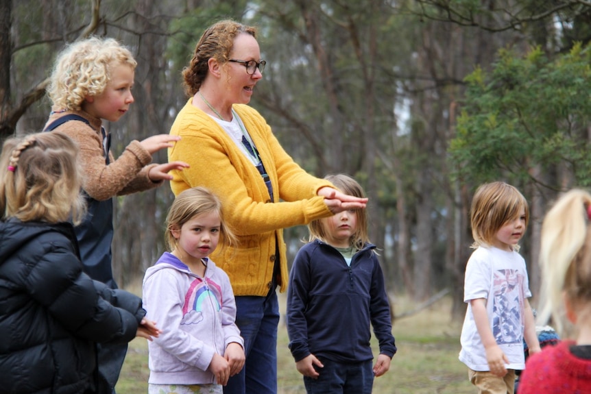 A school teacher stands with a group of primary school children in a bush setting