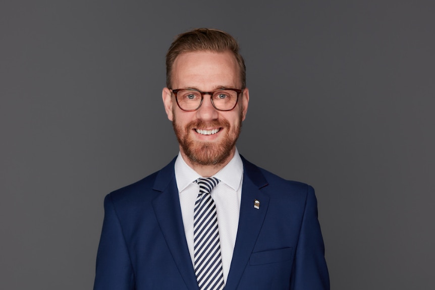 A man in a suit and glasses poses in front of a blank background