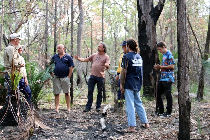 A group of men stand in a circle in the bush