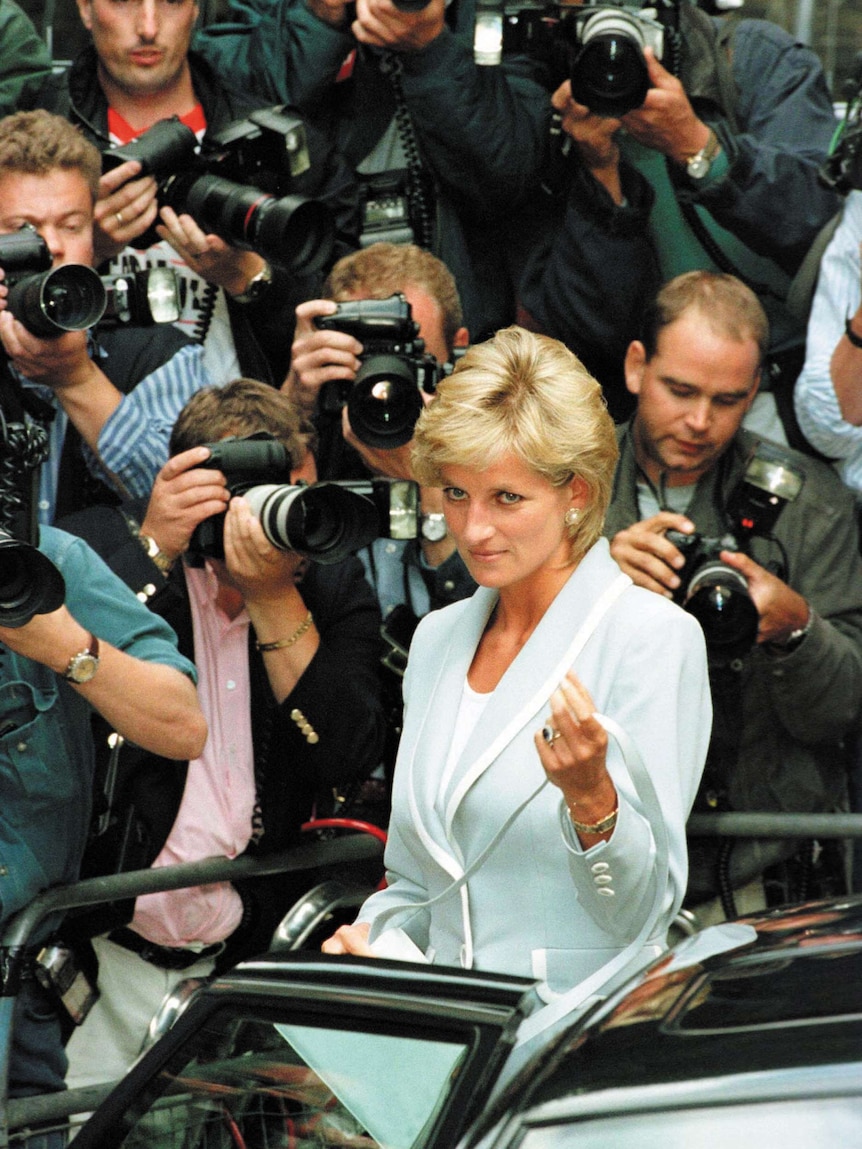 Princess Diana surrounded by camera people as she gets into a car.