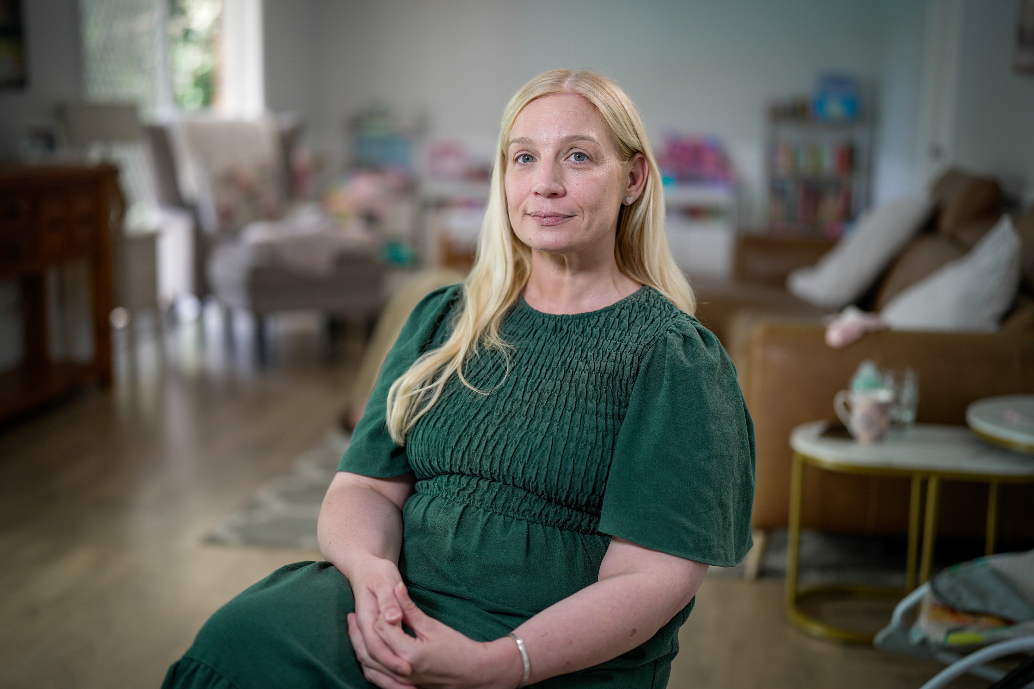 A woman in a green dress sits at her home looking at the camera.