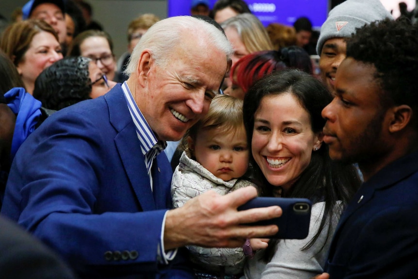 Joe Biden smiles with a phone in his hand with voters.
