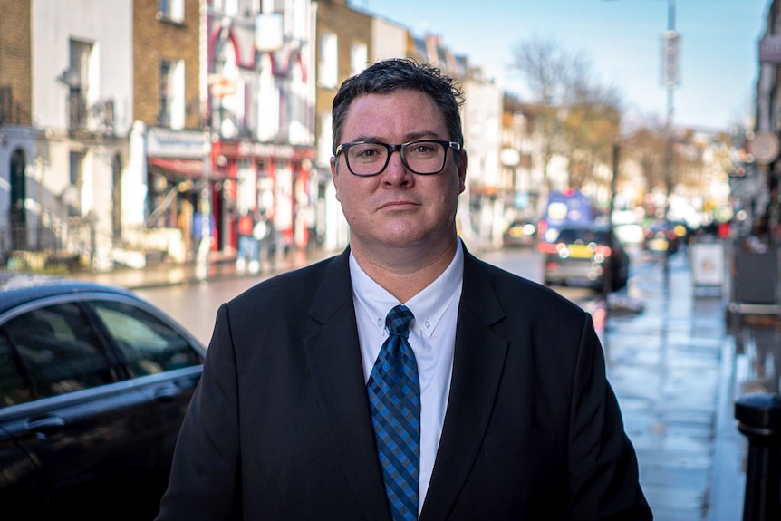 A man in glasses stands in a London street.