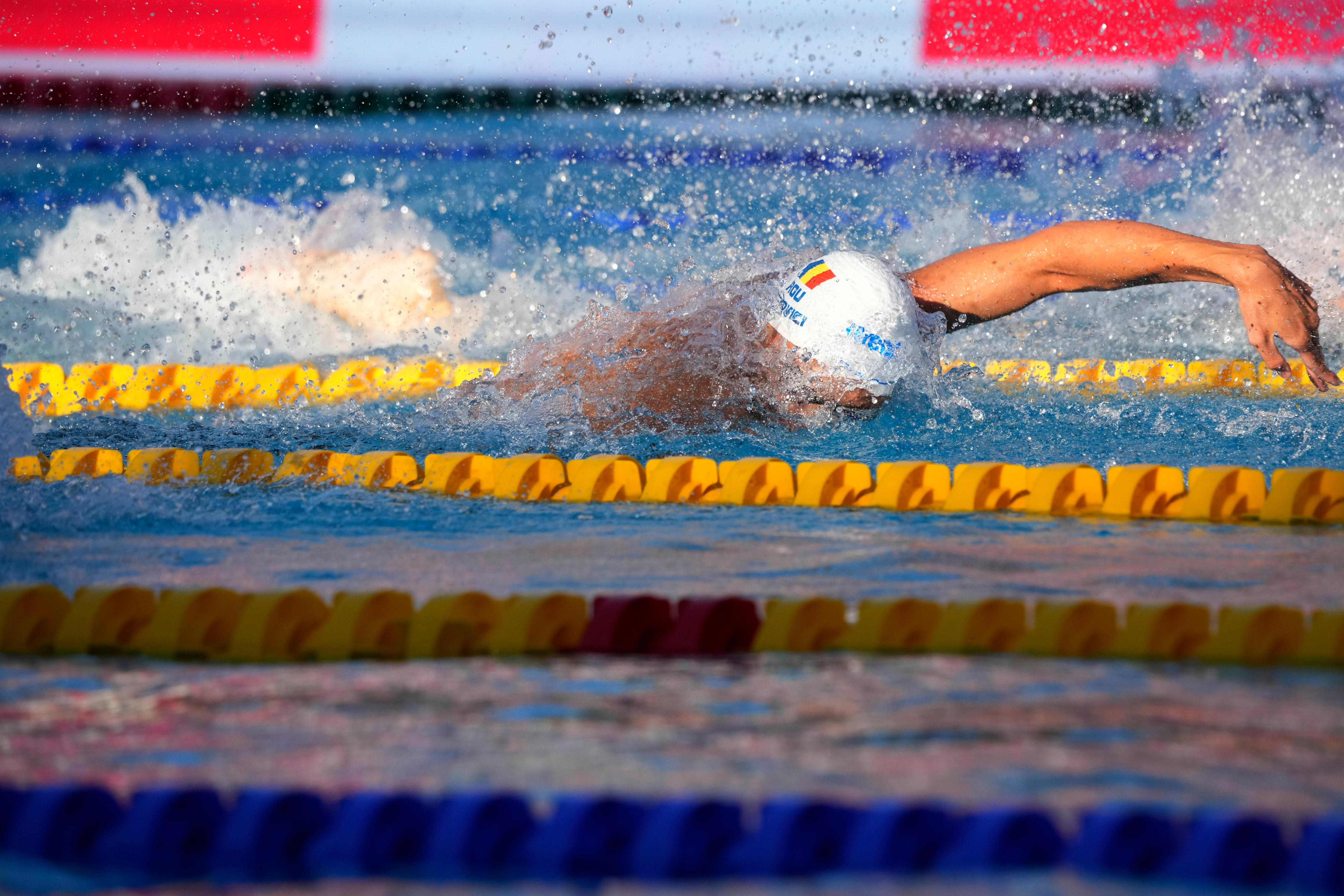 A Romanian swimmer stretches his arm out to pull himself through the water in a freestyle race.