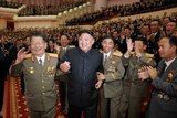 Kim Jong-un smiles in front of a huge crowd in a concert hall. They are celebrating the country's nuclear scientists.