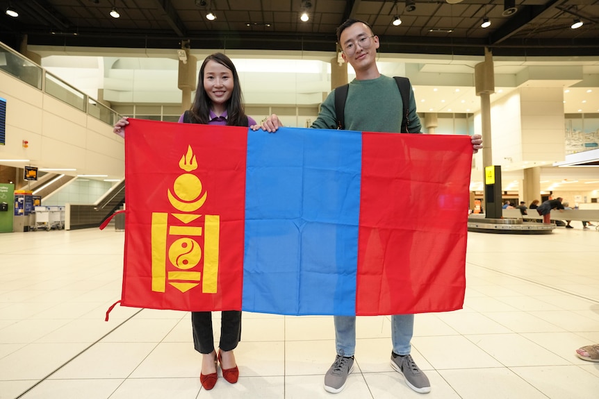Man and woman hold up mongolian flag at airport.