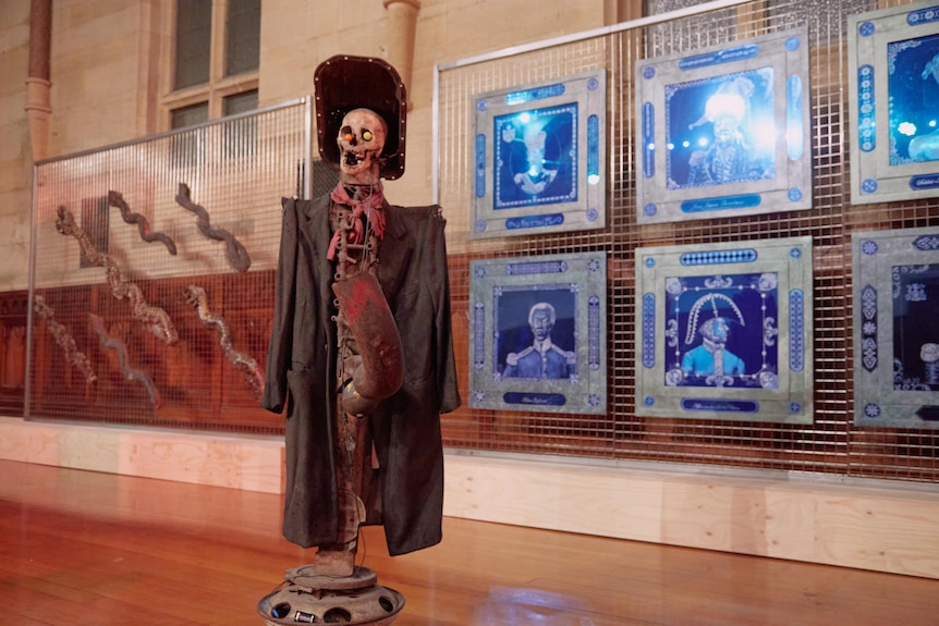 A skeleton mannequin sits on a stand, wearing an old trench coat and pirate-style hat.