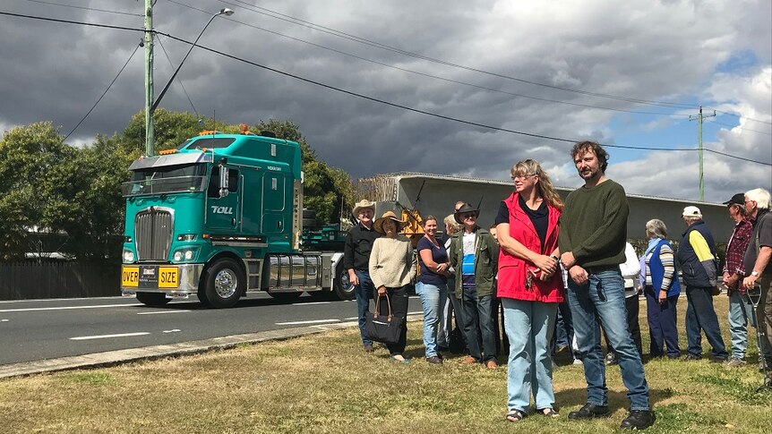 A group of residents standing beside a road with a B-Double truck passing behind them