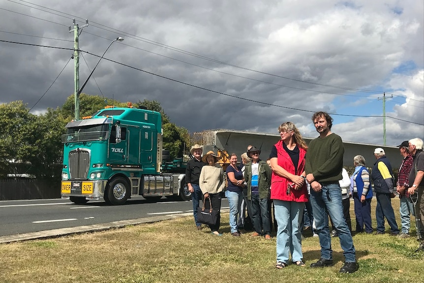 A group of residents standing beside a road with a B-Double truck passing behind them