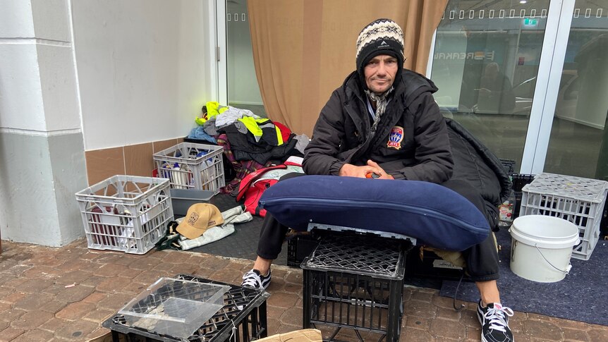 A homeless man sitting on milk crates in front of a disused shop.