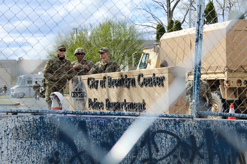 Three men in combat gear next to a sign reading 'City of Brooklyn Center Police Department'