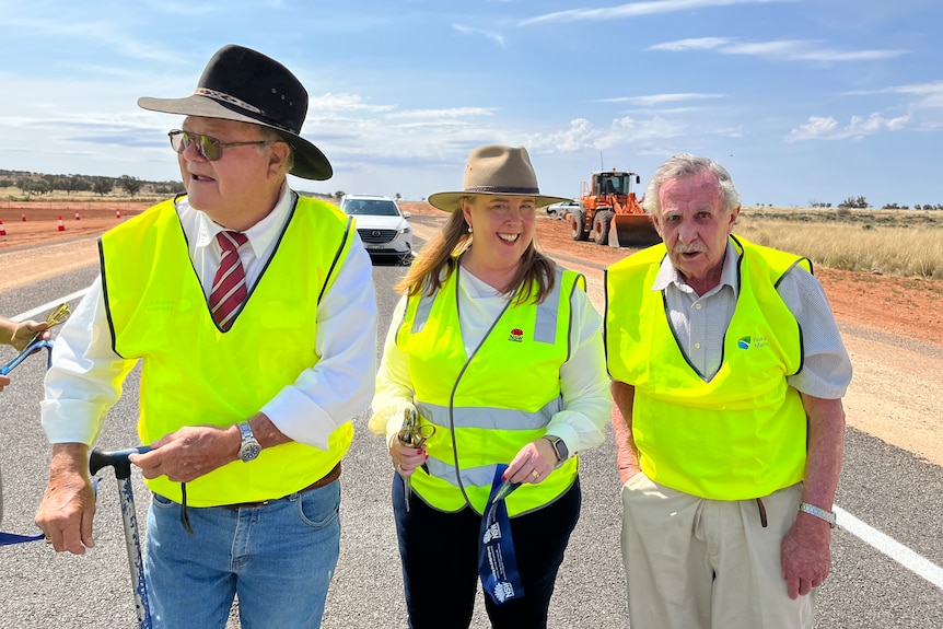Two older men and a woman standing in a line wearing fluro vests.