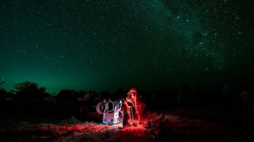 Astronomers looking at the night sky through a telescope.