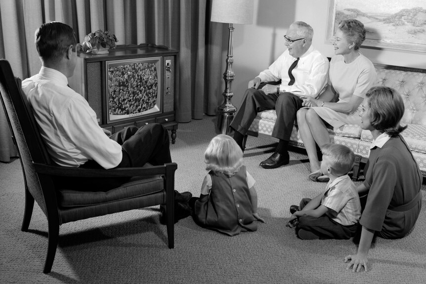  A black and white photo of a 1960s family watching television.
