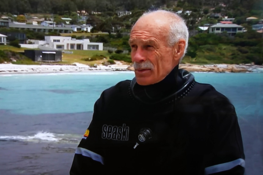 John Smith, of Bicheno, wearing a black jacket standing in front of the ocean at Bicheno.