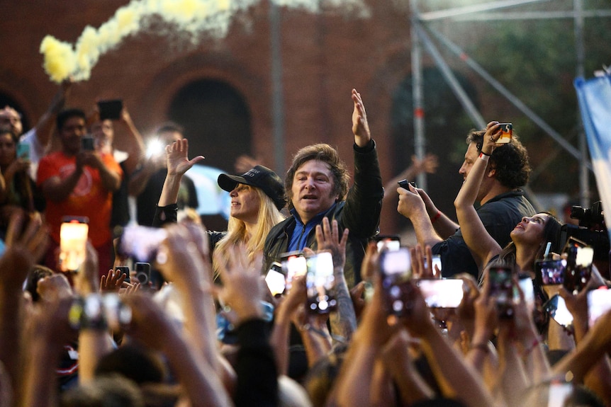 A man waves his hands in the air while looking over a crowd of people.
