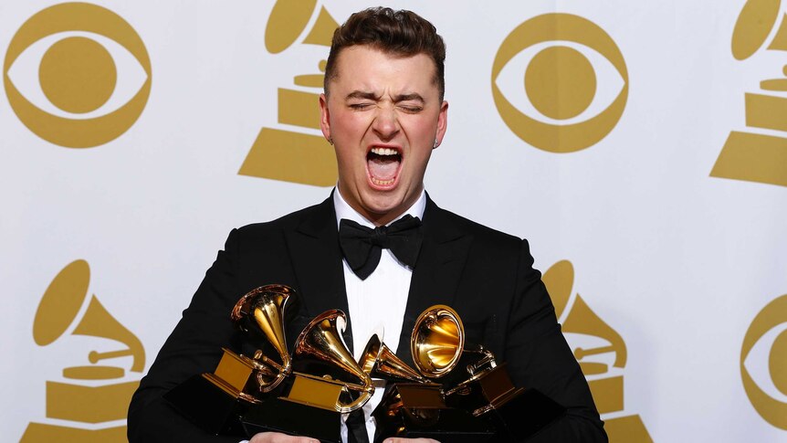 Pop star Sam Smith makes a funny face for the cameras while holding four Grammy awards in front of a media backdrop