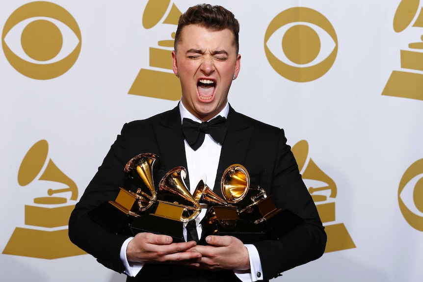 Pop star Sam Smith makes a funny face for the cameras while holding four Grammy awards in front of a media backdrop