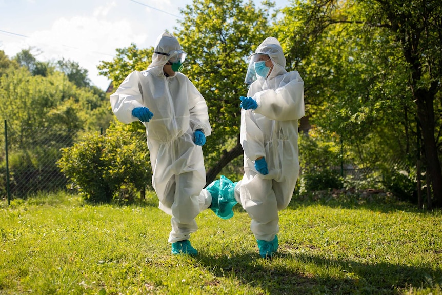 Two people in PPE gear joke around in a park.