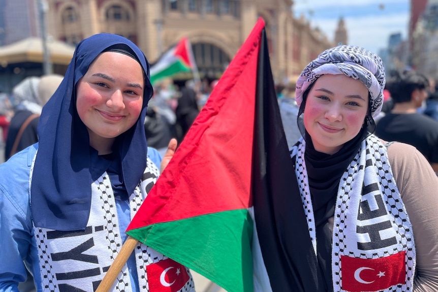 Two teenage girls holding a Palestinian flag outside Melbourne's Flinders Street Station.
