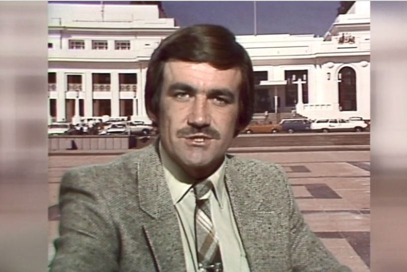 Cassidy in suit and tie presenting with Old Parliament House in Canberra in background.