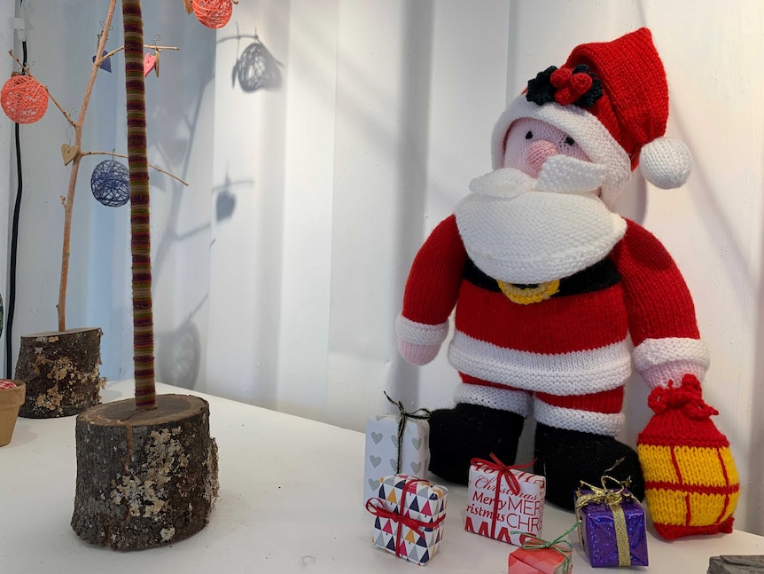 A knitted Santa sitting on a pedestal with some presents.