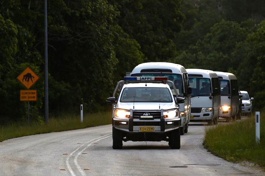 A head-on shot of an AFP vehicle leading a convoy of small white buses along a road on Christmas Island at dawn.